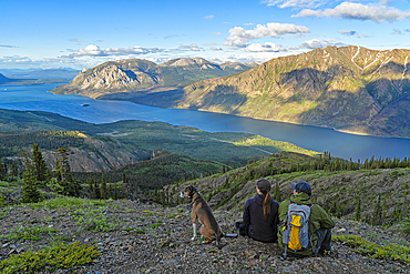 View taken from behind of two women sitting on a mountain top with their dog enjoying the view, while exploring and photographing the amazing scenery of the Yukon along the Sam McGee Trail near Carcross, Yukon, Carcross, Yukon Territory, Canada