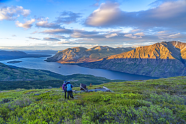 View taken from behind of two women standing on a mountain top with arms around shoulders, enjoying the view, while exploring and photographing the amazing scenery of the Yukon up along the Sam McGee Trail near Carcross, Yukon, Carcross, Yukon Territory, Canada