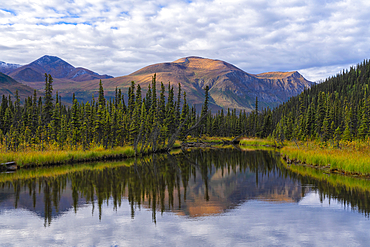 Scenic view of the serene wilderness at the end of a lake in the remote Yukon Territory with sunrise illuminating the mountain tops creating a beautiful reflection in the still waters, Yukon, Canada