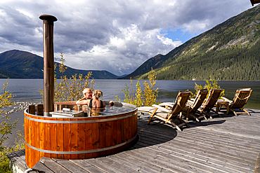 Couple sharing a tender moment while sitting in a wood fired hot tub on the shore of a Yukon Lake, Yukon, Canada