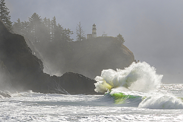 Morning fog enhances the dramatic beauty of the waves crashing into the cliffs at Cape Disappointment Lighthouse at the mouth of the Columbia River in Southwest Washington, Washington, United States of America