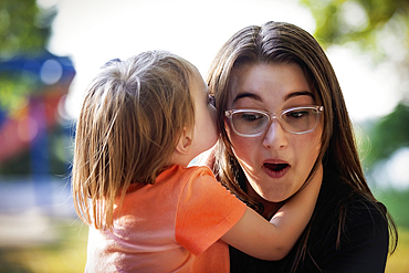 Older sister spending quality time with her little sister and listening to secrets, in a city park during a warm fall afternoon, Leduc, Alberta, Canada