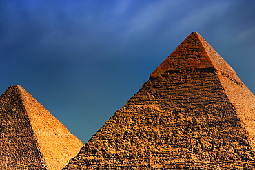 Two of the primary Pyramids of Giza, sunlit with a golden hue, the Great Pyramid (Khufu) under a dark, cloudy sky, Giza, Egypt