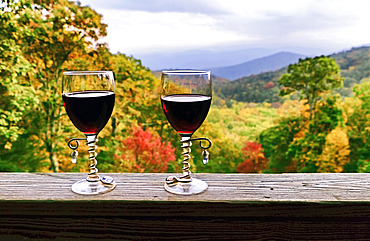 Two decorative glasses of red wine sit on a wooden railing above a mountain view in autumn, Fairview, North Carolina, United States of America