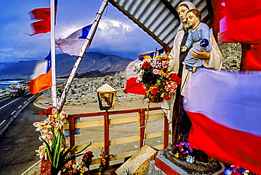 Flags and statuary decorate a colorful roadside altar in a desolate region of northern Chile. Shrines or animitas are a common tradition of memorials that mark the site where someone died. People who are not related to the person who was killed can offer a prayer at the animita, in this way, animitas can take the roles of popular saints in the Catholic religion, Pan American Highway, Chile