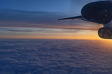 Stunning aerial view from an airplane, showing part of the wing and turbine engine, above the puffy clouds with a pastel sky at twilight, flight from Terrace to Vancouver, British Columbia, Canada