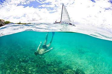 Split View of a teenage girl snorkeling in a bikini with a tour boat on the surface of the water above, Country of Aruba