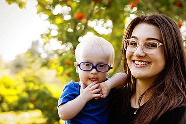 Outdoor portrait of an older sister spending quality time with her young brother who has Down Syndrome, in a city park during a warm fall afternoon, Leduc, Alberta, Canada