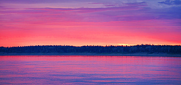 The evening sky ignites with colour as the sun goes below the horizon line in Fort Simpson. The Mackenzie River reflects the colour in a beautiful moment, Fort Simpson, Northwest Territories, Canada