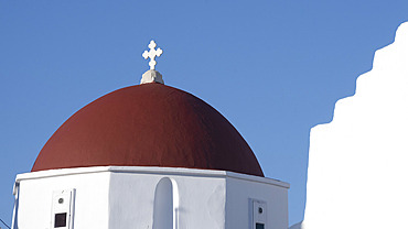 Cross and red dome on a whitewash church against a bright blue sky on the island of Mykonos, Mykonos, South Aegean, Greece