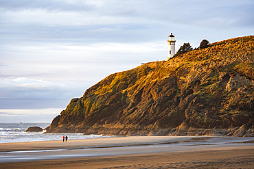 A couple walking on the beach below the North Head Lighthouse at Cape Disappointment State Park near the mouth of the Columbia River, Washington State, Washington, United States of America