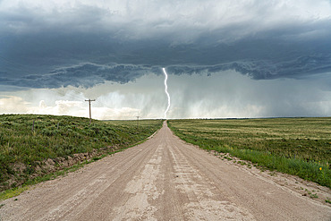 Lightning bolt strikes from a thunderstorm while a lonely road leads into the storm, Kansas, United States of America