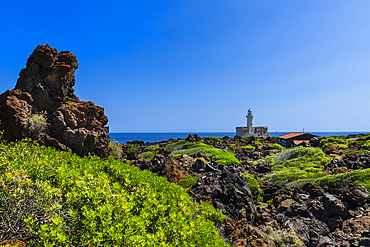 Scenic view of the coastal landscape with volcanic rock formations and the Lighthouse at Faro Di Punta Spadillo in the National Park of Pantelleria Island under a bright blue sky, Pantelleria Island, Trapani, Sicily, Italy