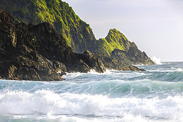 Rugged landforms covered in green vegetation and crashing surf along an Indonesian island at Telawas Beach, Mekar Sari, Praya Barat, Central Lombok Regency, West Nusa Tenggara, Indonesia