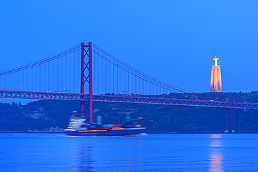 Container ship passing under the Bridge of 25 April and Almada Cristo Rei statue at sunset, Belem district, Lisbon, Portugal, Europe