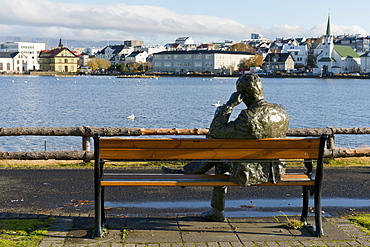 Sculpture of a man sitting on a park bench in front of Tjornin Lake and the Historic Centre of Rykjavik, Iceland, Polar Regions