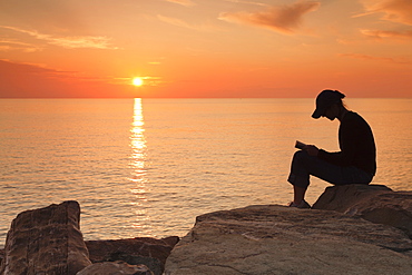 Woman sitting on the coast at sunset, reading, Corsica, France, Mediterranean, Europe