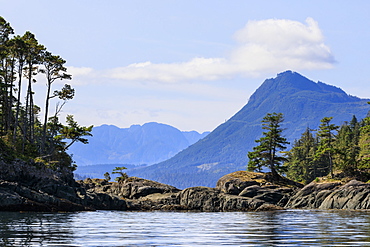 Tree lined rocky shore of an island in calm seas near Alert Bay, Inside Passage, British Columbia, Canada, North America, North America