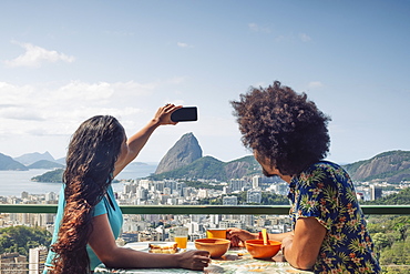 A multi-ethnic couple breakfasting and taking a mobile phone photo of Sugar Loaf and the Rio skyline, Rio de Janeiro, Brazil, South America