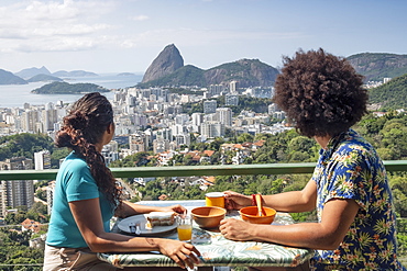 A multi-ethnic couple breakfasting together and looking out over Sugar Loaf mountain and the Rio skyline, Rio de Janeiro, Brazil, South America