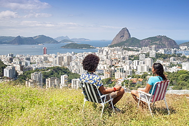 A multi-ethnic couple sitting together and looking out over Sugar Loaf mountain and the Rio skyline, Rio de Janeiro, Brazil, South America