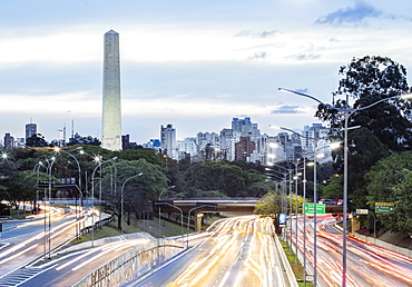 Rush hour traffic light trails on 23 de Maio Avenue, the skyline and the Obelisk of Heroes in Ibirapuera Park, Sao Paulo, Brazil, South America