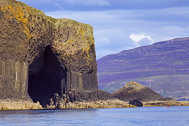 Fingal's Cave, the hexagonal mouth of the cave with the heather-covered slopes of Mull behind, Argyll and Bute, Scotland, United Kingdom, Europe