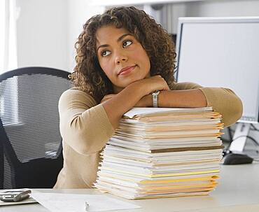 African businesswoman leaning on stack of paperwork