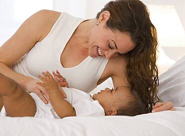 Hispanic mother playing with baby on bed