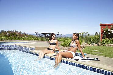 Multi-ethnic women with feet in swimming pool