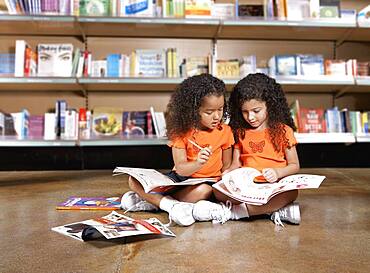 Two young sisters reading books in library