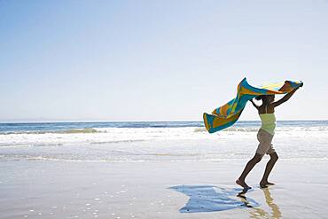 African girl holding beach towel in wind