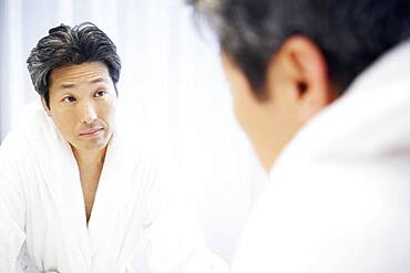 Asian man looking in bathroom mirror