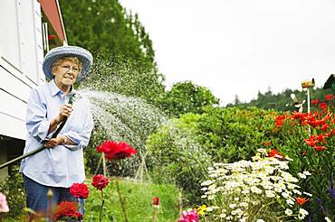 Senior woman watering plants with hose