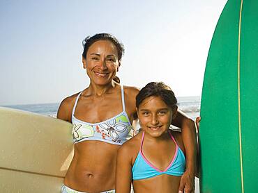 Hispanic mother and daughter holding surfboards