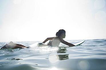 Hispanic girl paddling on surfboard