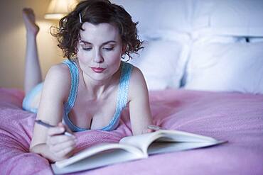 Woman laying on bed with pen and book