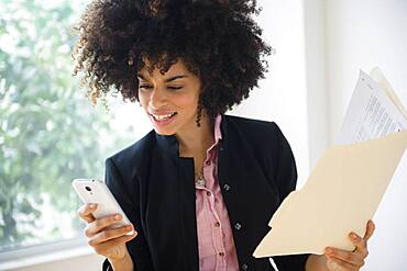 Mixed race businesswoman using cell phone near window