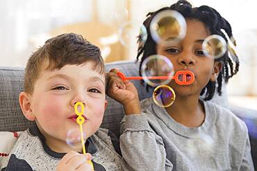 Close up of boys blowing bubbles on sofa