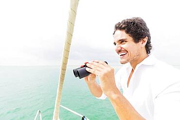 Hispanic man looking out from boat deck with binoculars