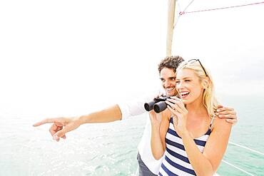 Couple looking out from boat deck with binoculars