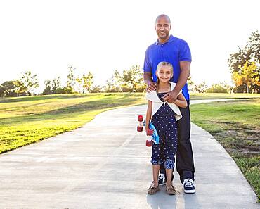 Father and daughter hugging with skateboard in park