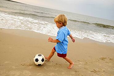 Caucasian boy playing with soccer ball on beach