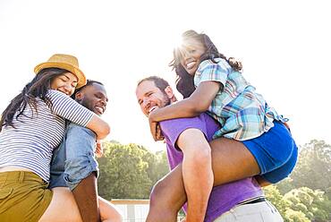 Men carrying girlfriends piggyback outdoors