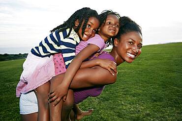 Mother carrying children piggyback in park