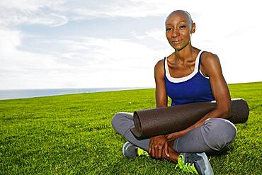 African American woman holding yoga mat in park