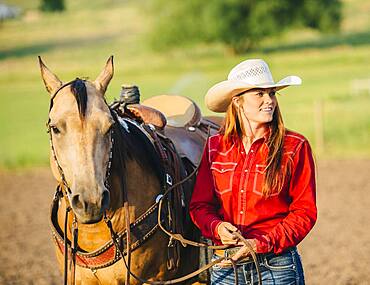 Caucasian cowgirl walking horse on ranch