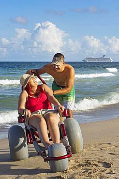 Man pushing paraplegic girlfriend in wheelchair on beach