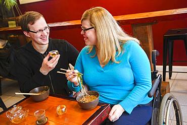 Paraplegic woman and boyfriend eating noodles in tea shop