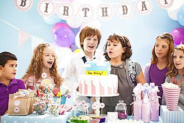 Children blowing out candles on birthday cake at party